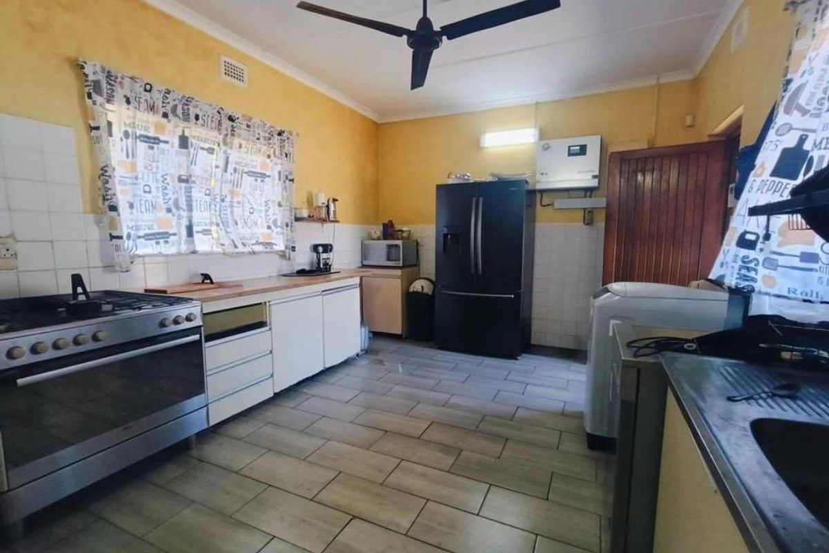 A functional kitchen featuring tiled flooring, a gas stove, and built-in cabinetry with a tiled splashback and ceiling fan.