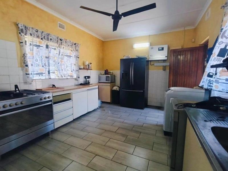 A functional kitchen featuring tiled flooring, a gas stove, and built-in cabinetry with a tiled splashback and ceiling fan.