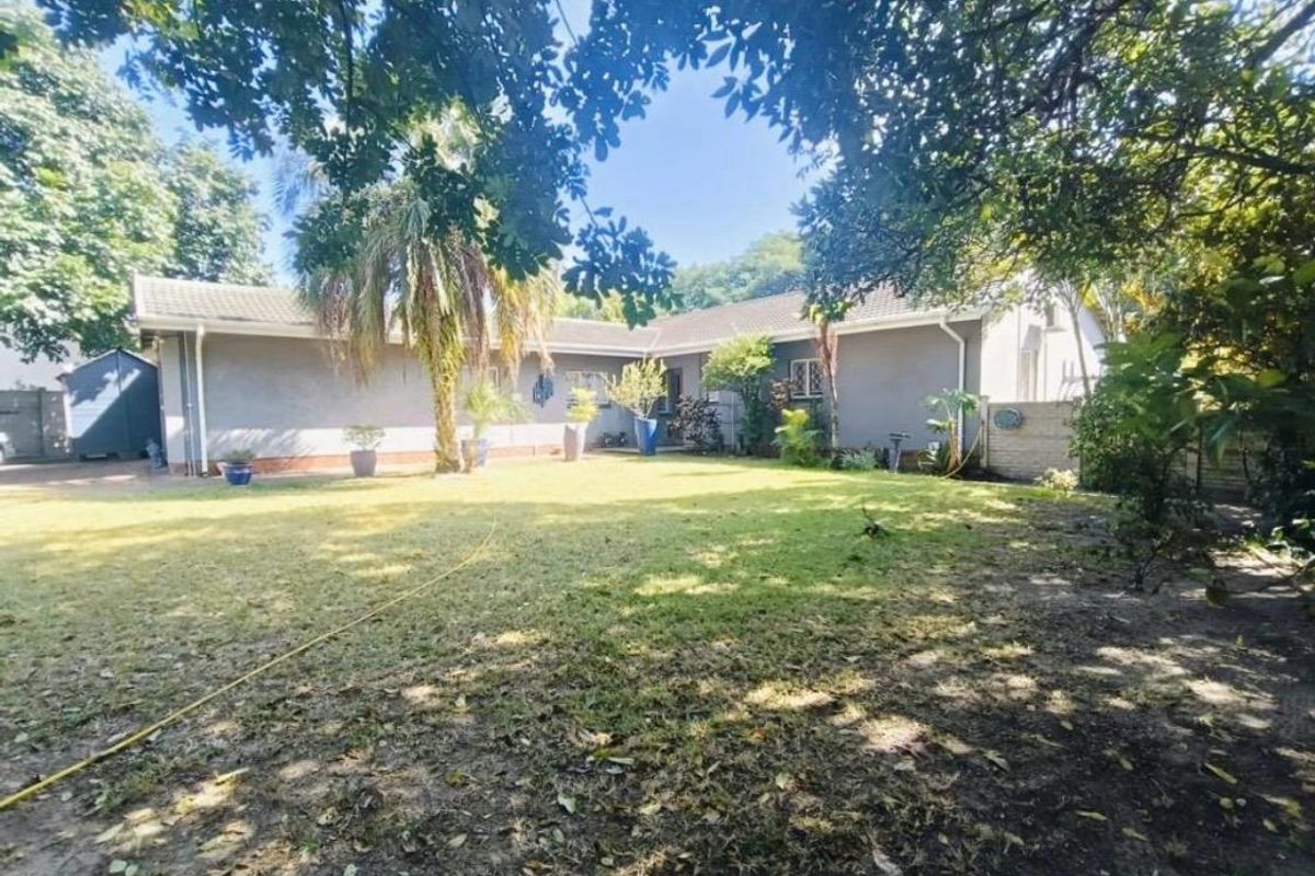 A view of the rear exterior of the house featuring a spacious garden, mature trees, and a plastered facade.