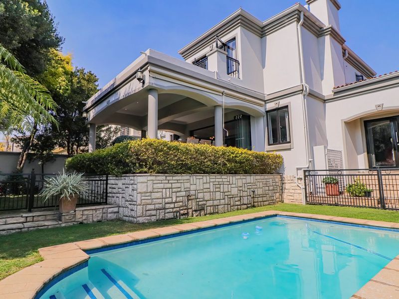 Rear exterior view featuring a swimming pool, stone retaining wall, and a spacious covered patio area perfect for outdoor entertaining.