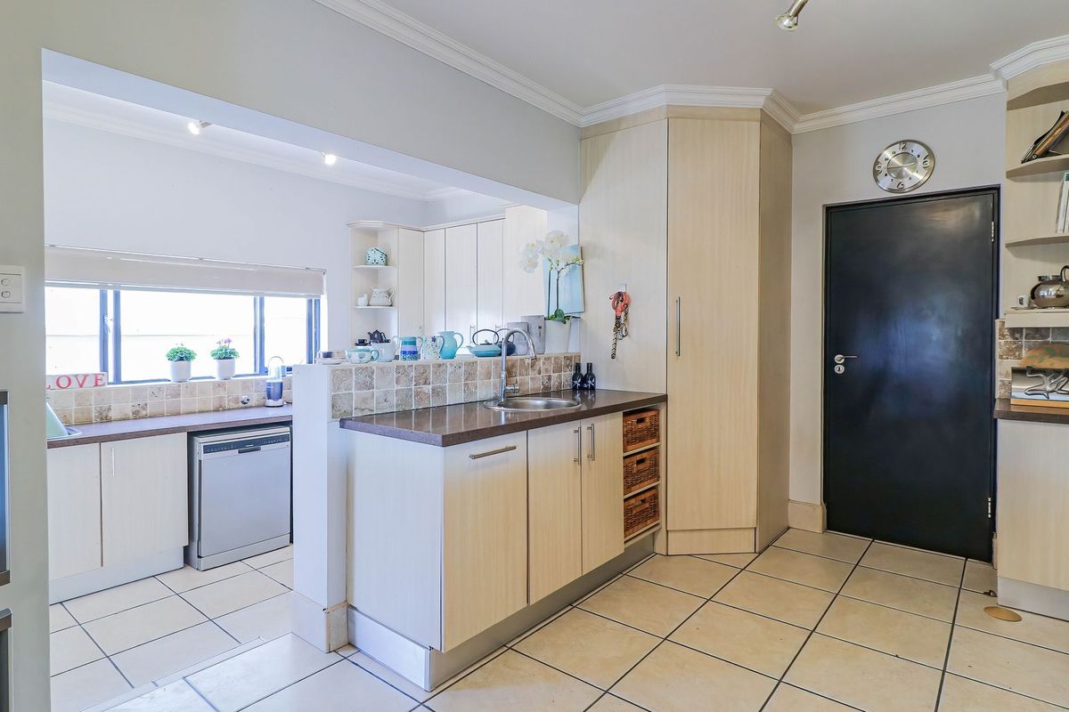 A functional kitchen featuring light wood-finish cabinetry, tiled countertops and backsplash, integrated dishwasher, and tiled flooring with a clean, open-plan layout.