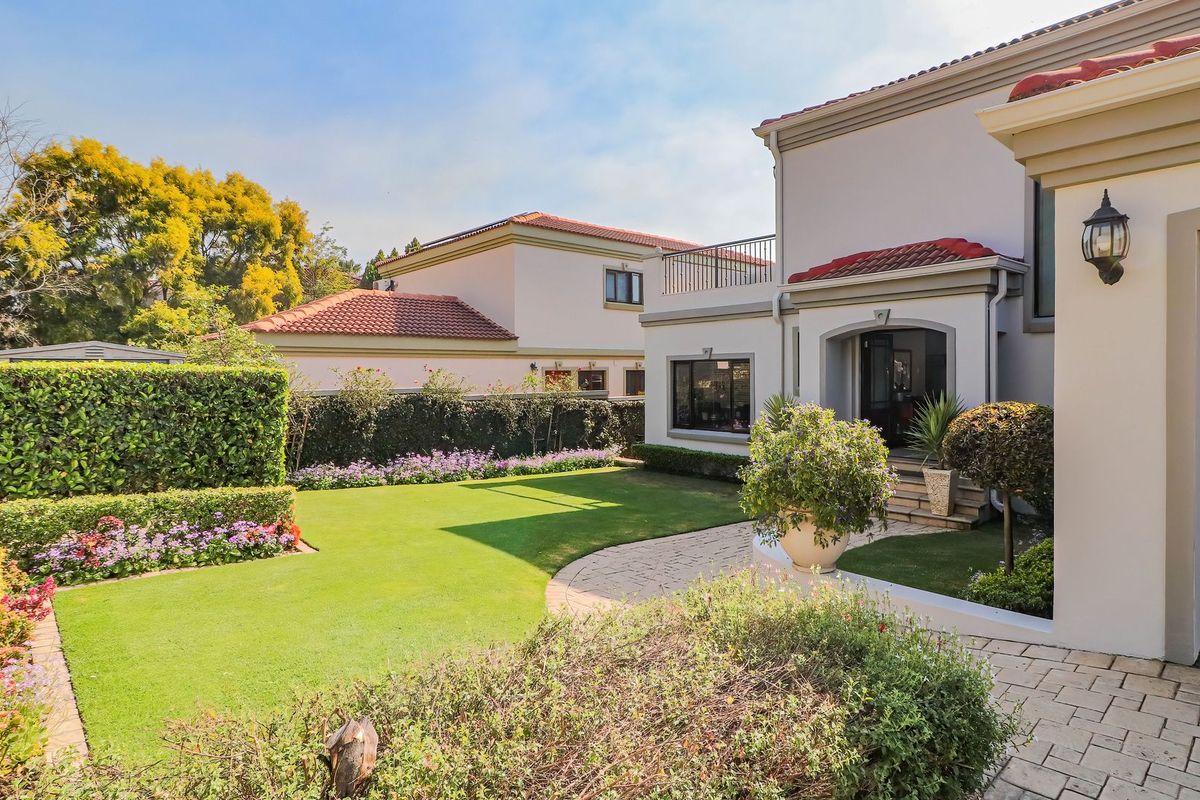 A well-maintained rear garden featuring a manicured lawn, paved pathway, and established landscaping, adjacent to the main dwelling with a balcony.