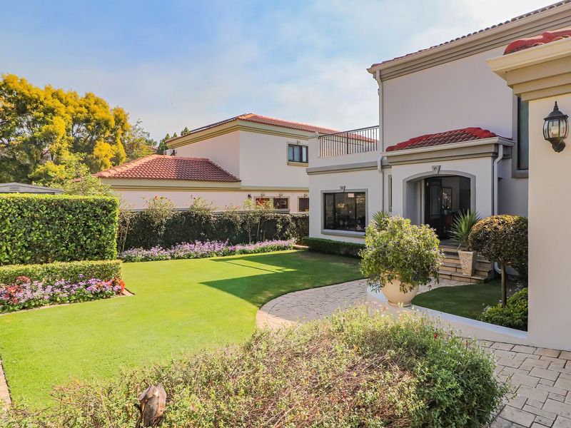 A well-maintained rear garden featuring a manicured lawn, paved pathway, and established landscaping, adjacent to the main dwelling with a balcony.