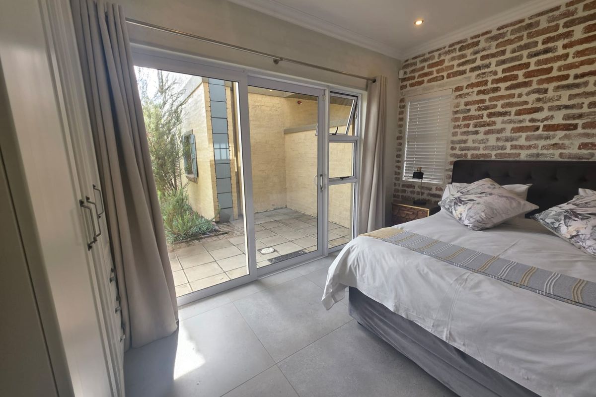 A well-maintained bedroom featuring an exposed brick accent wall, large sliding glass doors leading to a private patio, and modern tiled flooring.
