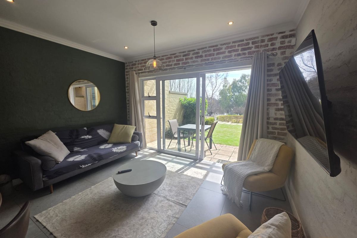 A bright living room featuring an exposed brick feature wall, large sliding glass doors leading to a patio, and modern tiled flooring.