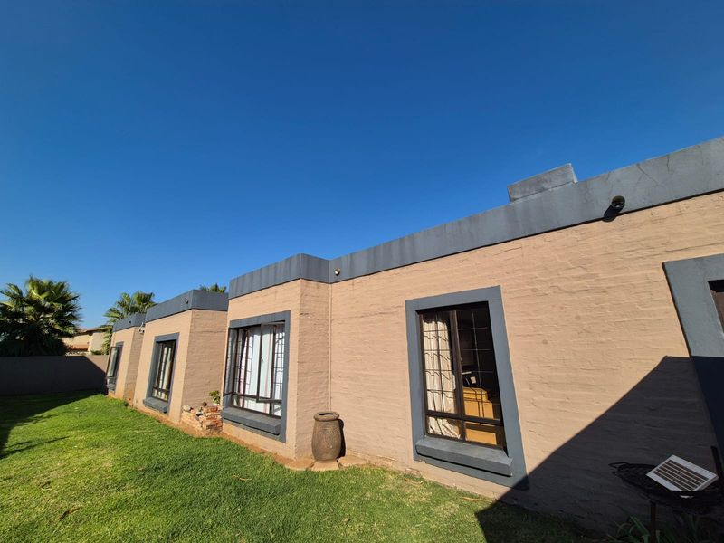 Rear exterior view of the house featuring a painted brick facade, security bars on windows, and a well-maintained lawn area.