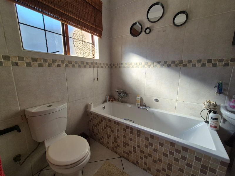 A functional bathroom featuring a built-in bathtub, toilet, and basin with neutral wall and floor tiling.