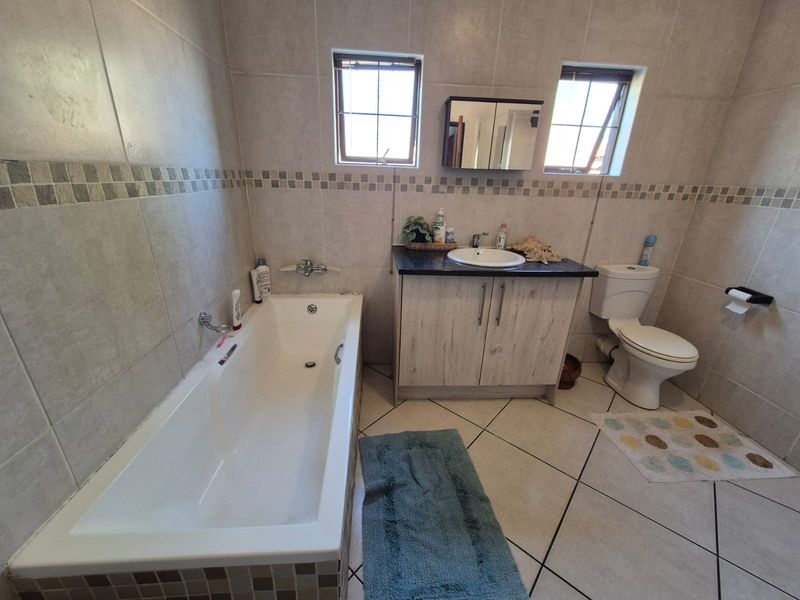 A functional bathroom featuring a built-in bathtub, vanity cabinet with countertop basin, wall-mounted mirror cabinet, and tiled finishes throughout.