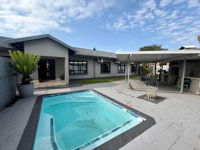 Outdoor entertainment area featuring a swimming pool, paved patio, and a covered patio with a built-in braai.