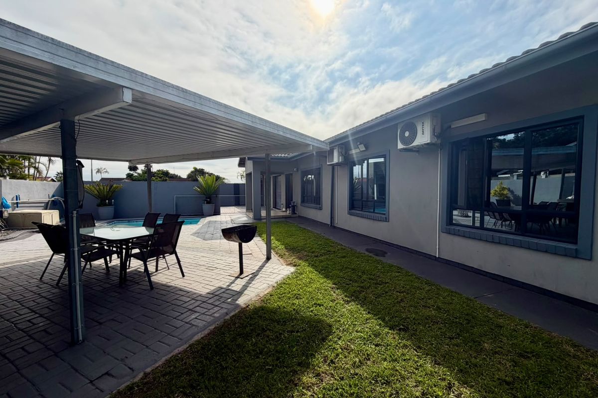 Rear exterior view featuring a covered patio, paved entertainment area, swimming pool, and a well-maintained lawn alongside the townhouse structure.