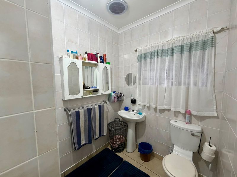 A functional bathroom featuring a pedestal basin, toilet, and wall-mounted medicine cabinet, finished with neutral wall and floor tiles.