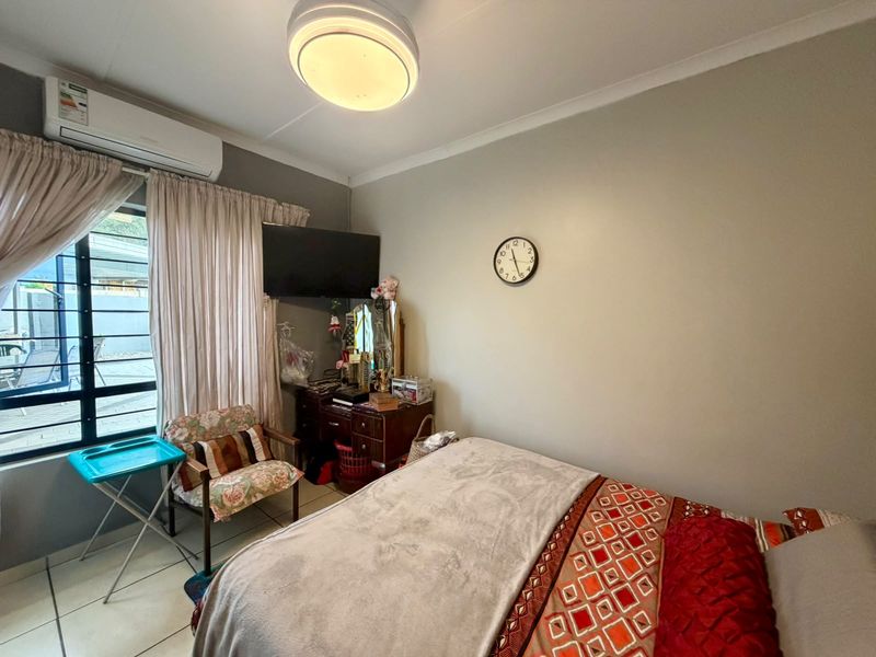 A functional bedroom featuring tiled flooring, an installed air conditioning unit, and a window with security bars.