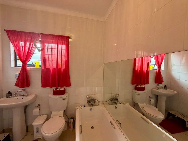 A functional bathroom featuring a pedestal basin, toilet, and bathtub with full-height wall tiling and a large vanity mirror.