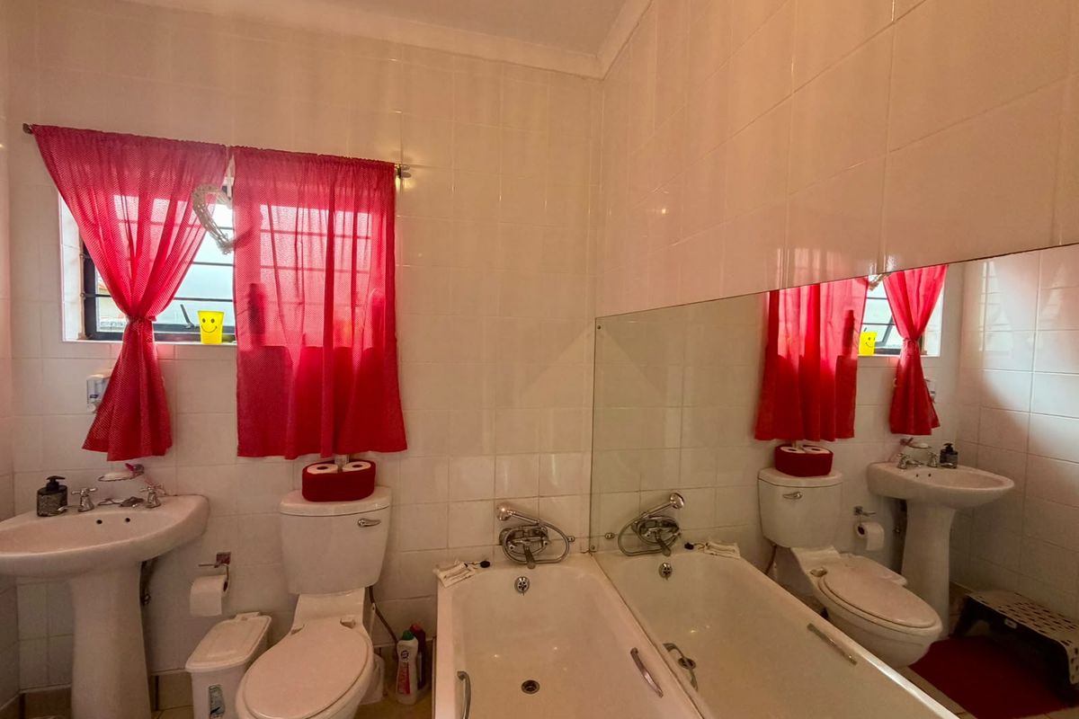A functional bathroom featuring a pedestal basin, toilet, and bathtub with full-height wall tiling and a large vanity mirror.