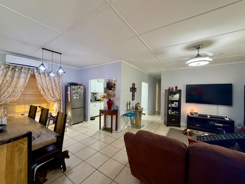 Open-plan living and dining area featuring tiled flooring, a split-system air conditioner, and a ceiling fan, with an adjacent kitchen access point.