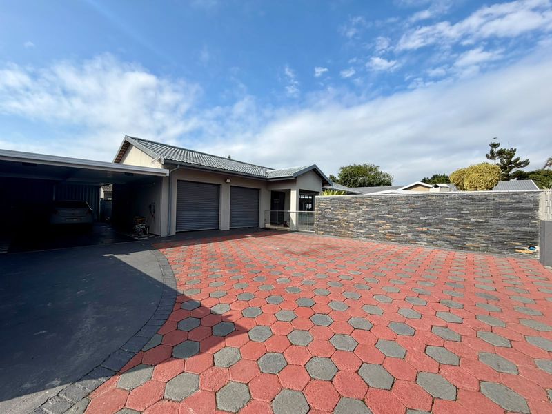Front exterior view of the townhouse featuring a double garage, attached carport, and a decorative stone-clad boundary wall with a paved driveway.
