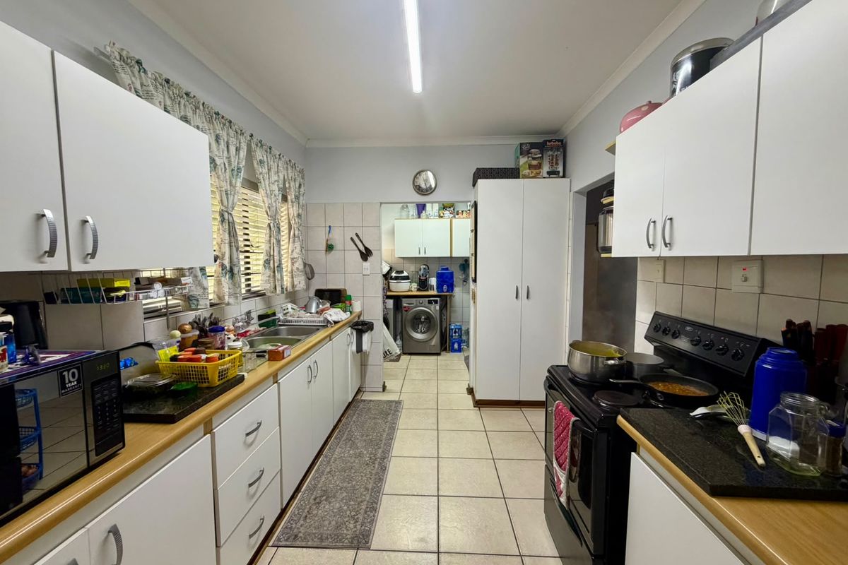 Functional kitchen featuring white cabinetry, laminate countertops, tiled splashbacks, and a dedicated scullery area with laundry plumbing connections.