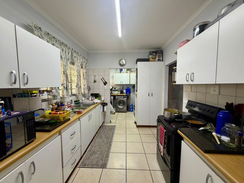 Functional kitchen featuring white cabinetry, laminate countertops, tiled splashbacks, and a dedicated scullery area with laundry plumbing connections.