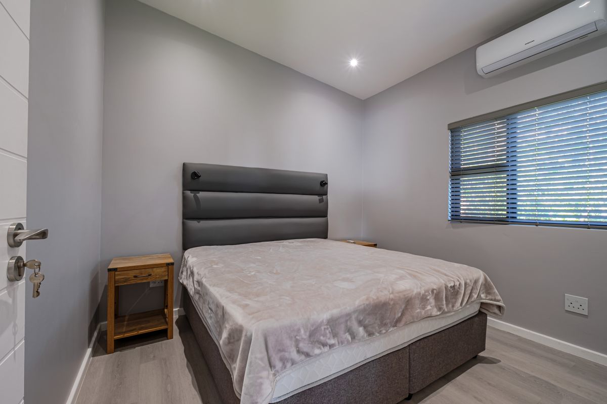 A well-maintained bedroom featuring neutral grey walls, laminate flooring, an integrated air conditioning unit, and modern recessed lighting.
