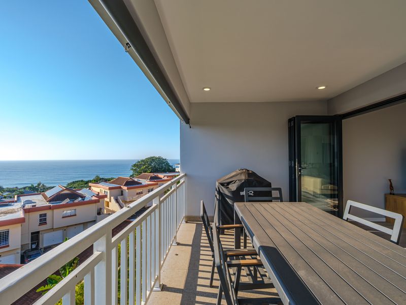 Spacious covered balcony featuring tiled flooring, recessed lighting, and a metal balustrade, offering expansive ocean views and seamless indoor-outdoor flow through bi-fold doors.