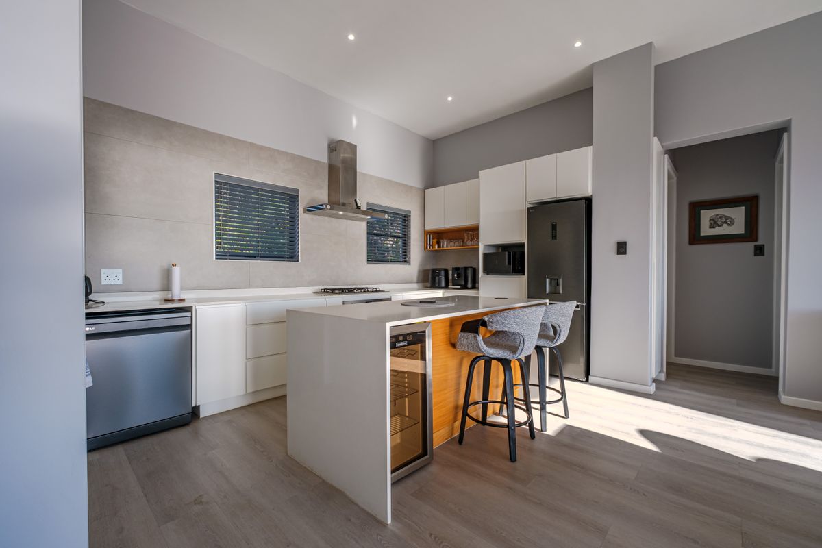 Modern kitchen featuring a central island with integrated wine cooler, sleek white cabinetry, stone countertops, and high-quality built-in appliances.