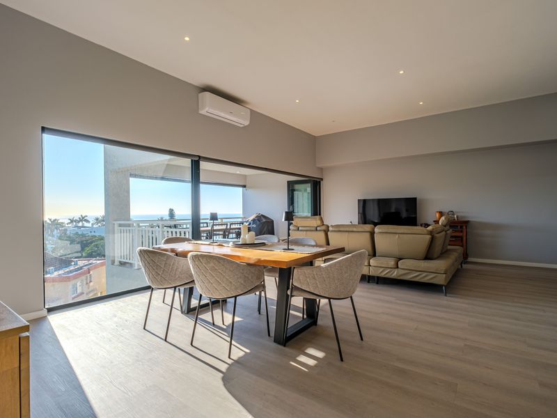 Spacious open-plan living and dining area featuring modern laminate flooring, recessed lighting, air conditioning, and large sliding doors opening to a balcony with views.