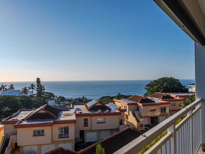 A scenic elevated view of the ocean and surrounding residential complex, captured from a private balcony.