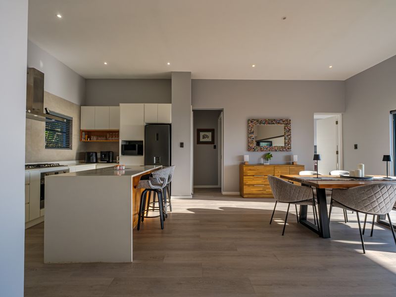 Modern open-plan living area featuring a sleek kitchen with a central island, integrated appliances, and high-quality laminate flooring throughout the dining and kitchen space.