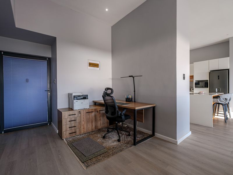An open-plan living area featuring a dedicated workspace nook and a modern kitchen with integrated appliances and sleek cabinetry.