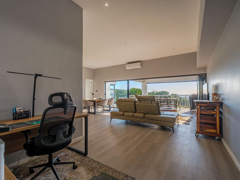Spacious open-plan living area featuring modern laminate flooring, recessed lighting, and large sliding glass doors that open onto a balcony with scenic views.