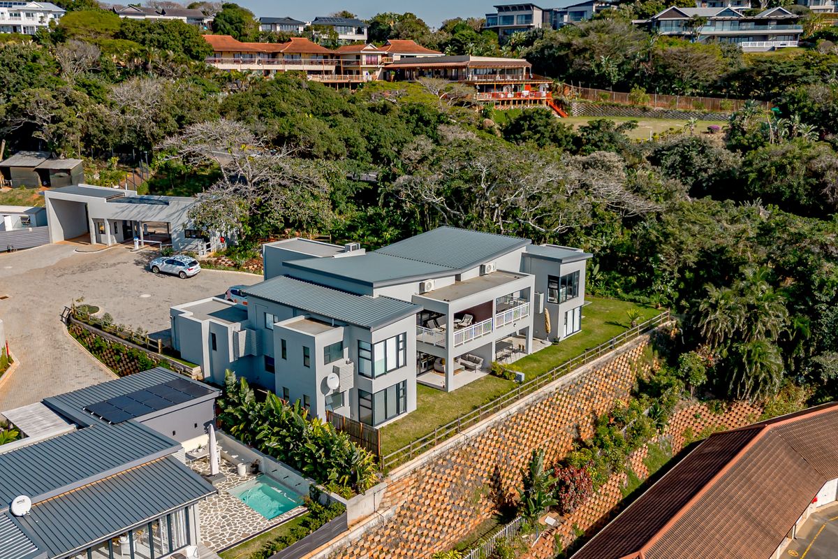 Aerial view of a modern multi-story apartment complex featuring metal roofing, private balconies, a swimming pool, and landscaped grounds with retaining walls.