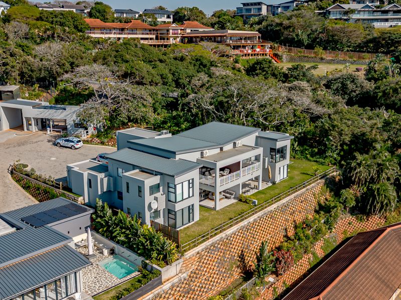 Aerial view of a modern multi-story apartment complex featuring metal roofing, private balconies, a swimming pool, and landscaped grounds with retaining walls.