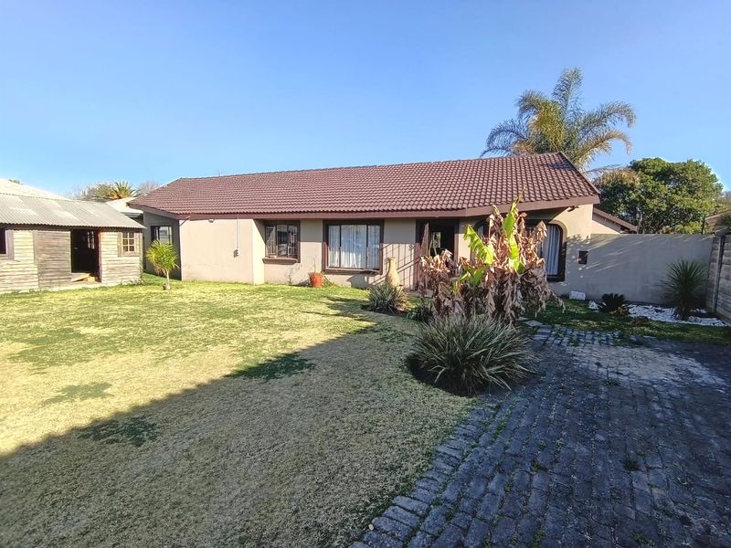 Rear view of the property featuring a tiled roof, paved driveway, and a detached outbuilding set within a spacious garden area.
