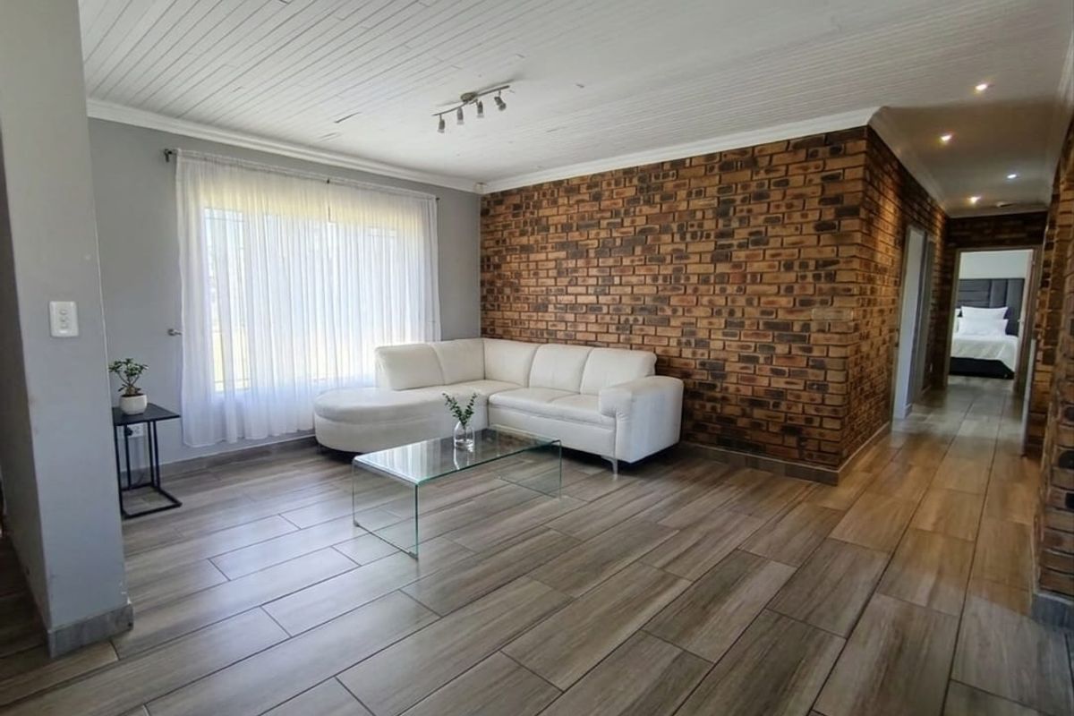 Spacious living room featuring a striking exposed brick accent wall, modern wood-look tile flooring, and a classic tongue and groove ceiling.
