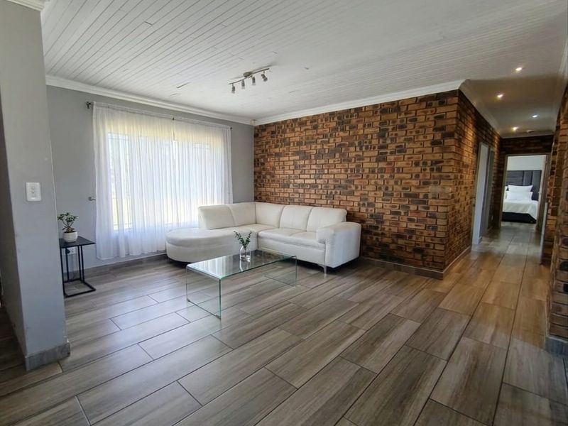 Spacious living room featuring a striking exposed brick accent wall, modern wood-look tile flooring, and a classic tongue and groove ceiling.