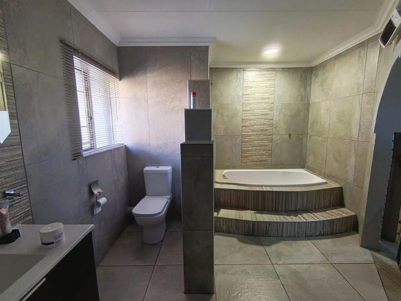 Modern bathroom featuring a raised built-in bathtub, tiled walls, a toilet, and a vanity with neutral finishes.