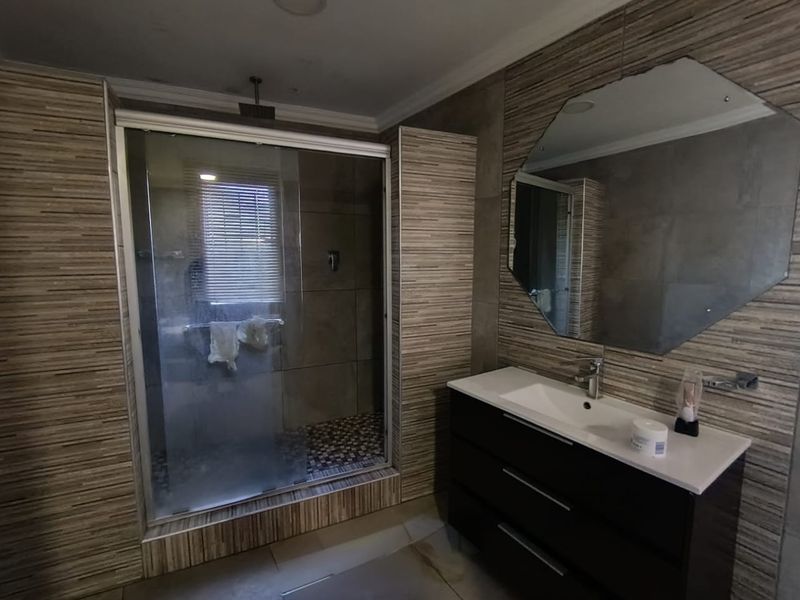 A modern bathroom featuring a walk-in shower with a glass enclosure, a vanity cabinet with a basin, and a large wall-mounted mirror.