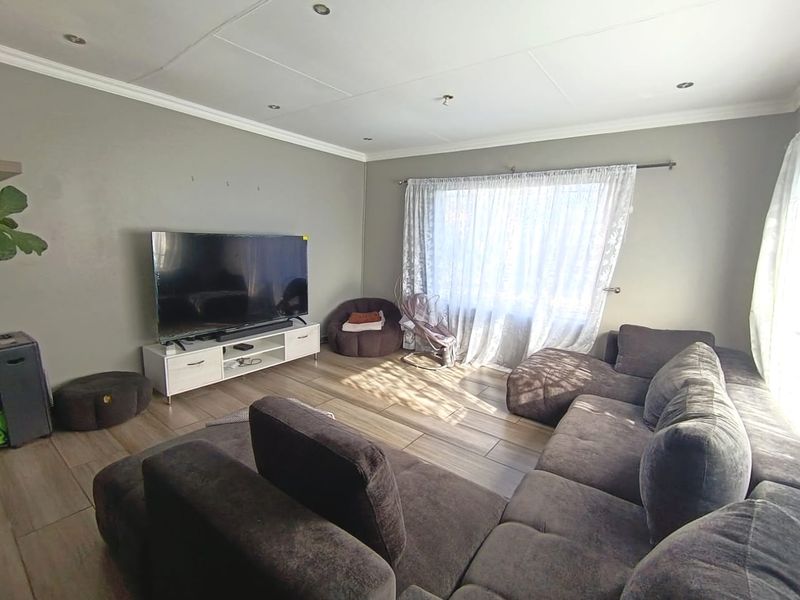 A comfortable living room featuring tiled flooring, recessed downlighting, and decorative cornicing, providing a neutral and functional space for relaxation.
