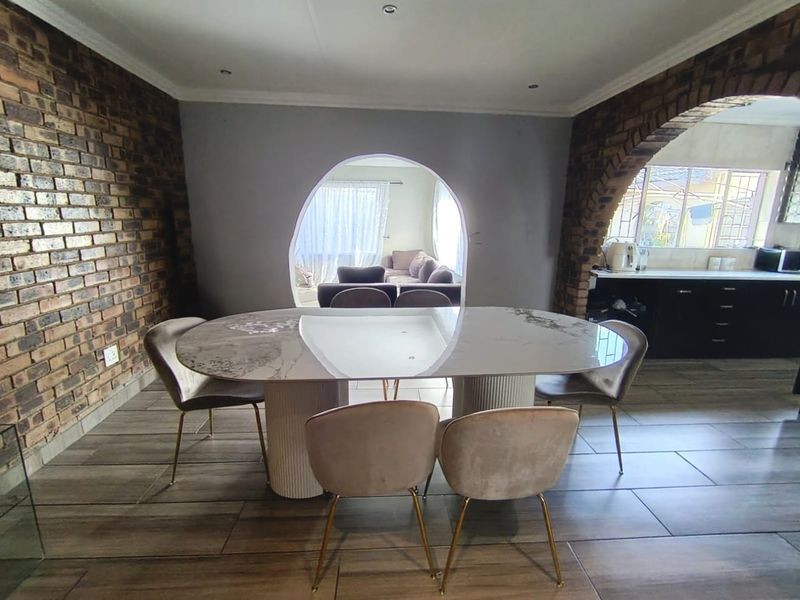 Open plan dining area featuring exposed brick walls, arched architectural details, and tiled flooring, seamlessly connecting to the adjacent kitchen and living space.