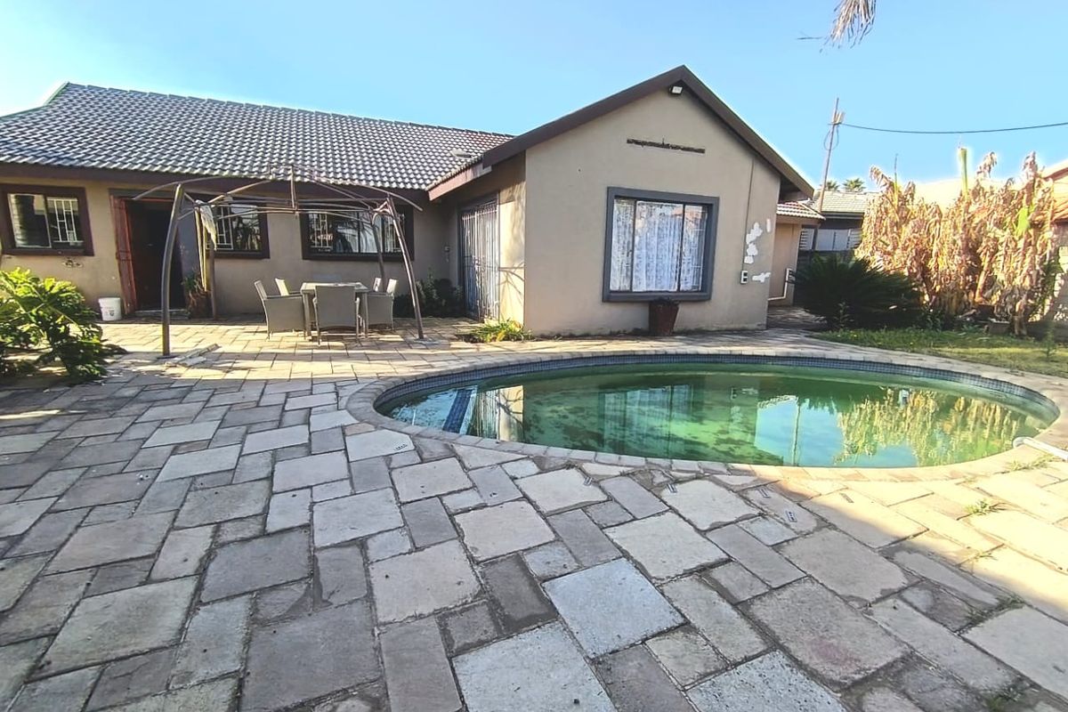 Rear exterior view featuring a paved patio area and a swimming pool, with visible wear to the building facade and pool maintenance required.