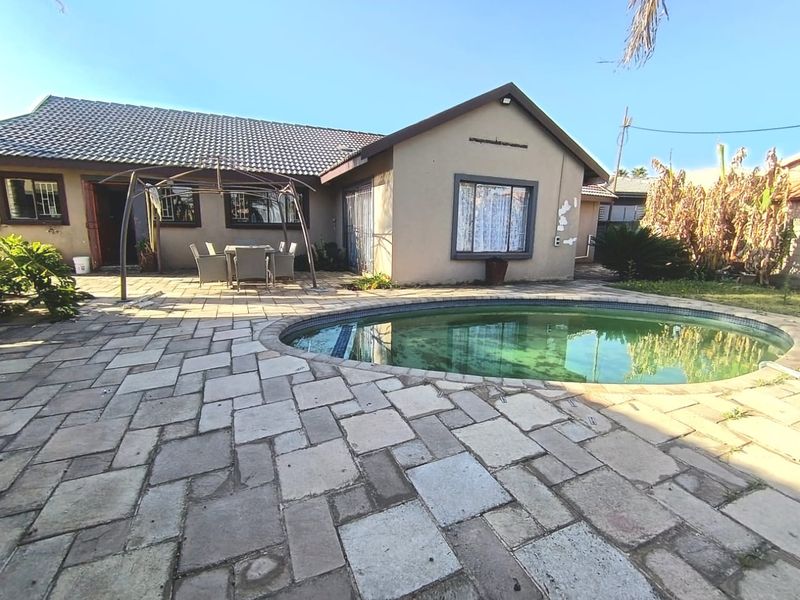 Rear exterior view featuring a paved patio area and a swimming pool, with visible wear to the building facade and pool maintenance required.