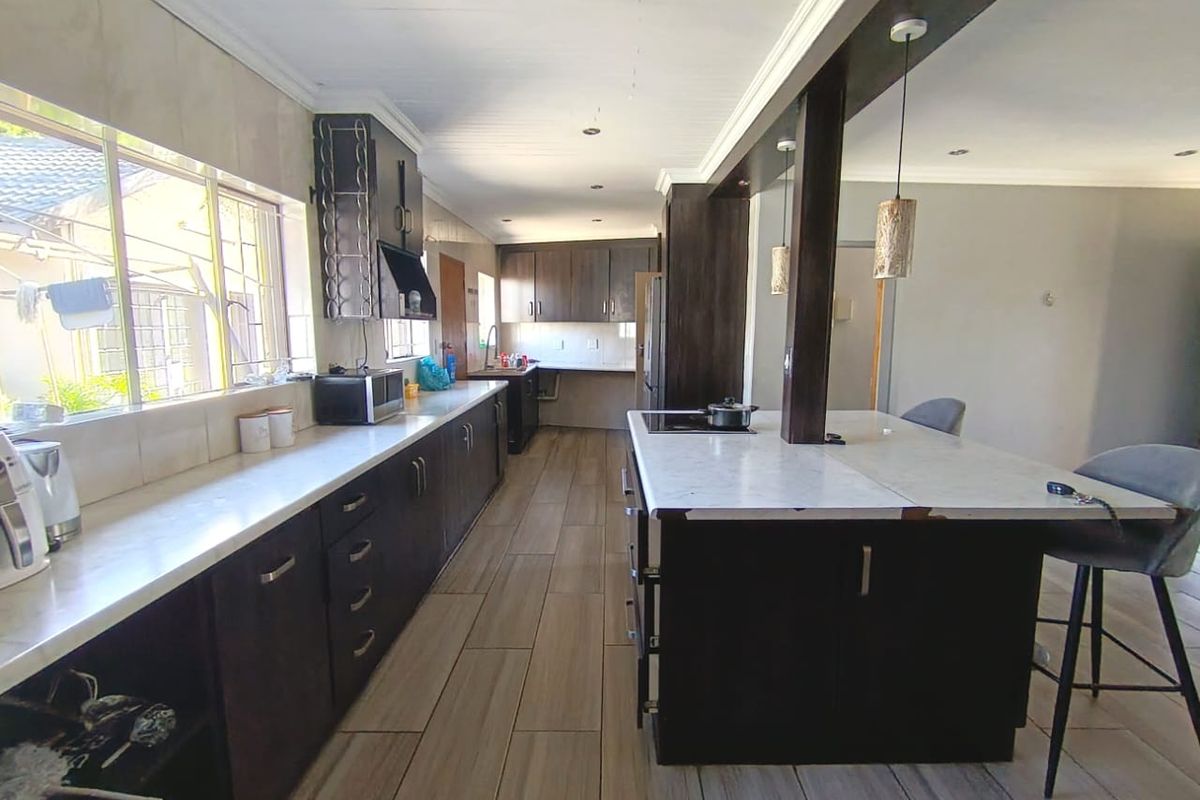 Modern kitchen featuring dark wood cabinetry, stone countertops, a central island with breakfast bar seating, and tiled flooring throughout.
