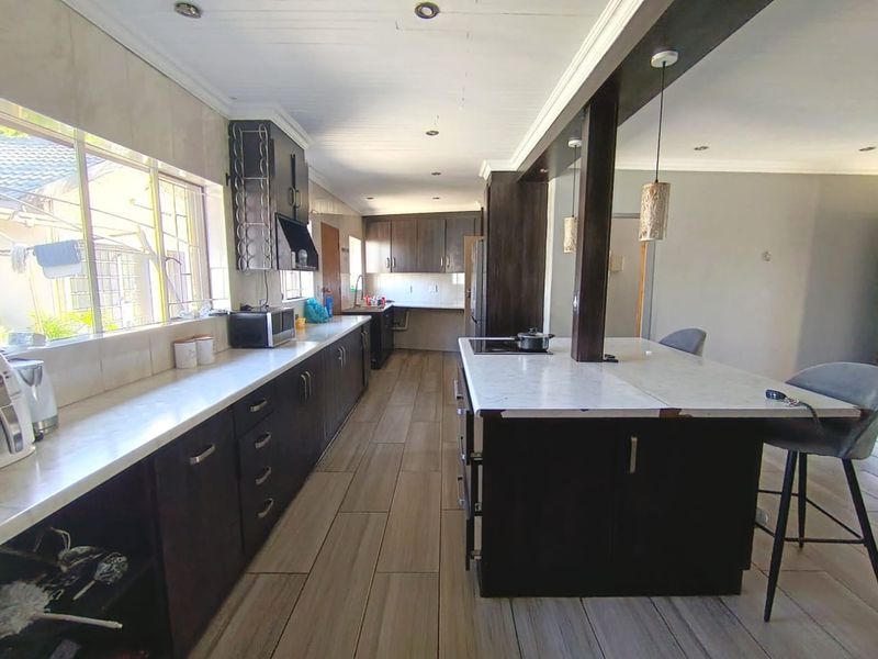 Modern kitchen featuring dark wood cabinetry, stone countertops, a central island with breakfast bar seating, and tiled flooring throughout.