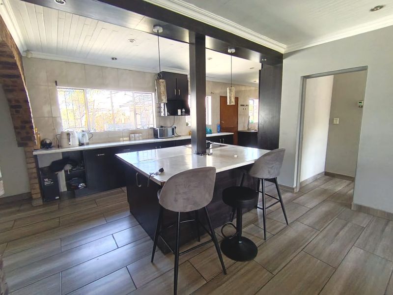 Modern kitchen featuring a central island with stone countertops, dark cabinetry, tiled flooring, and a timber ceiling with integrated lighting.