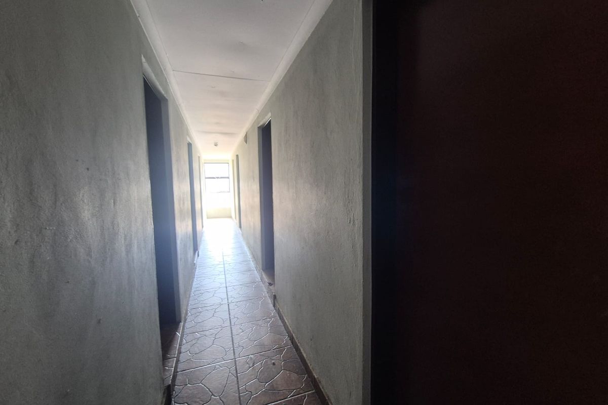 A narrow residential hallway featuring tiled flooring and multiple doorways leading to various rooms, requiring cosmetic updates to improve the overall finish.
