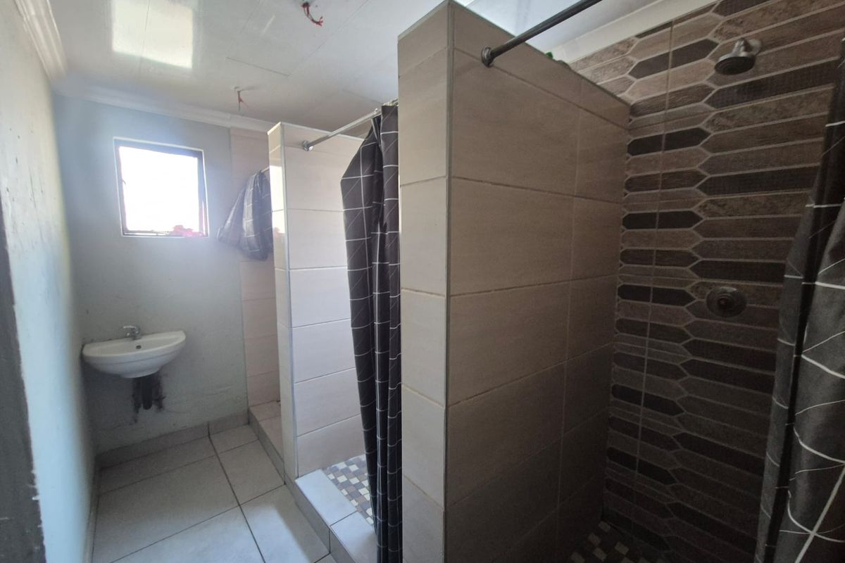 A functional bathroom featuring a wall-mounted basin and a tiled shower enclosure, currently requiring minor finishing touches to plumbing and electrical fixtures.