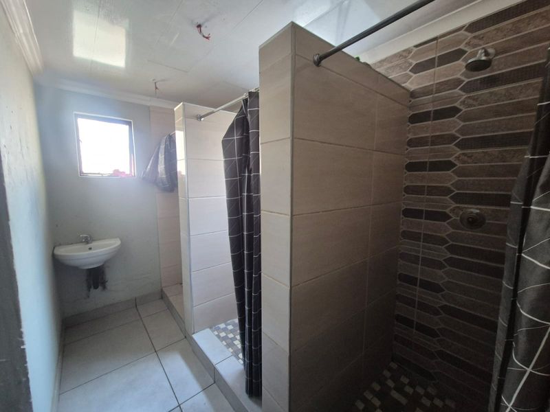 A functional bathroom featuring a wall-mounted basin and a tiled shower enclosure, currently requiring minor finishing touches to plumbing and electrical fixtures.
