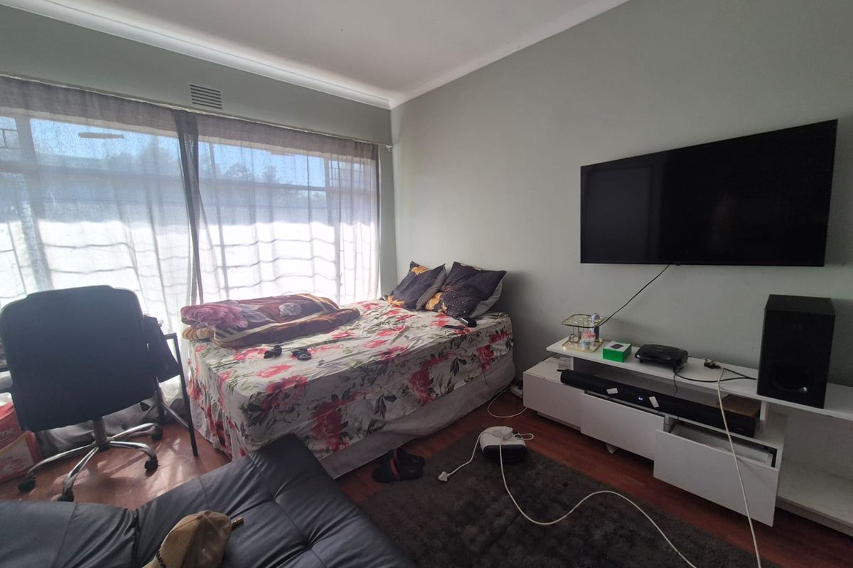 A bedroom featuring laminate flooring and a large window, providing natural light. The space includes a wall-mounted television setup.
