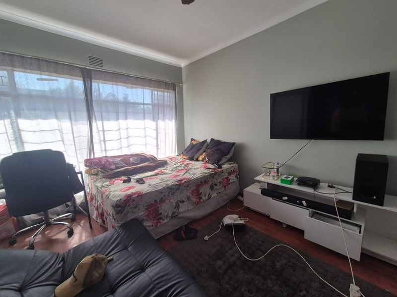A bedroom featuring laminate flooring and a large window, providing natural light. The space includes a wall-mounted television setup.