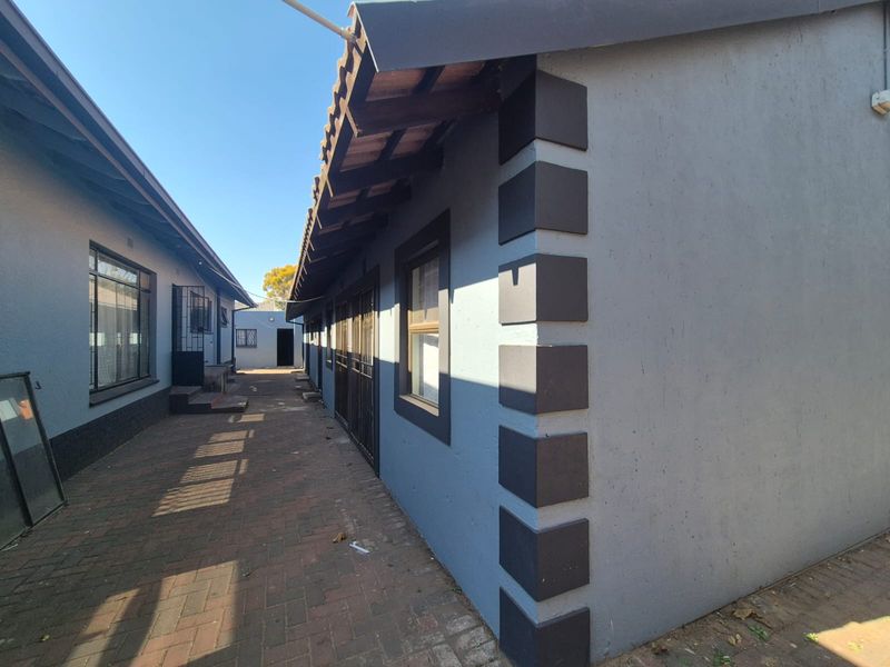 A side view of the property showing a paved walkway between two building structures with tiled roofing and security gates.